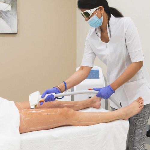Aarti Jaitly performing a treatment in the Refresh Skin Centre clinic — wearing protective eyewear, mask, and clinical attire